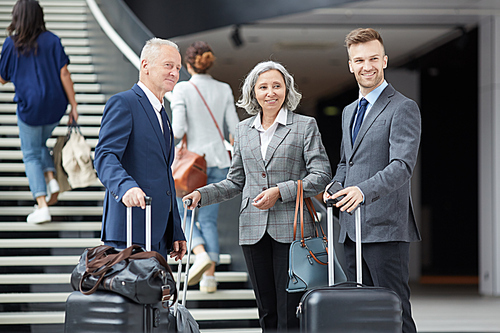 Group of positive multi-ethnic business people of different ages standing with luggage in airport and looking around