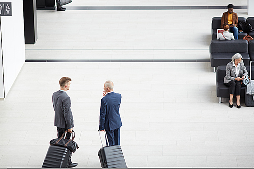 Directly above view of businessmen in suits holding handles of wheeled suitcases and discussing business trip in airport
