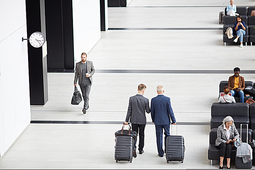 Above view of businessmen in suits carrying luggage and moving along airport while hurrying for boarding