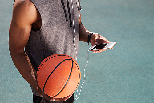 Mid section of unrecognizable African-American man holding basketball and using smartphone outdoors, copy space background