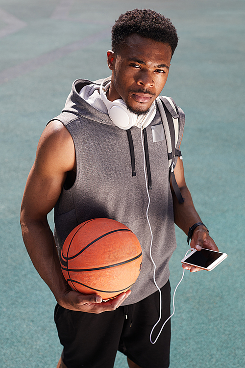 High angle portrait of handsome African-American man holding basketball and  in outdoor court