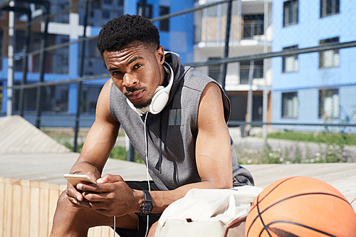 Portrait of handsome African-American man  while using smartphone in outdoor basketball court, copy space