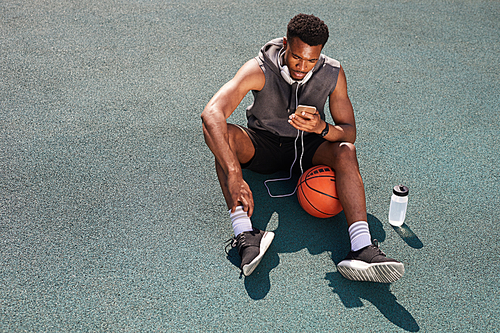 Above view background of handsome African-American man sitting in basketball court and using smartphone, copy space