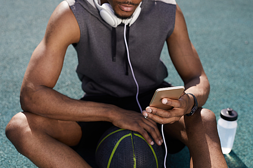 Mid-section background of contemporary African-American man using smartphone while sitting in basketball court, copy space