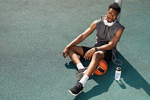 High angle portrait of handsome African-American man  while sitting in basketball court outdoors, copy space