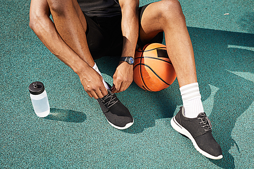 Low section portrait of contemporary African-American man tying sports shoes in basketball court outdoors, copy space background