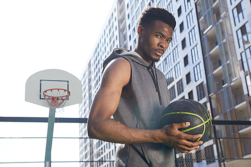Waist up portrait of handsome African-American man holding basketball ball and  confidently, copy space