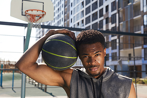 Portrait of handsome African-American man holding basketball ball  while posing in sports court outdoors, copy space