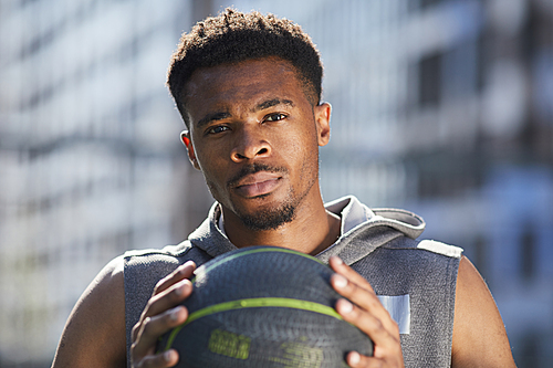 Head and shoulders portrait of handsome African man holding basketball ball in outdoor court and , copy space