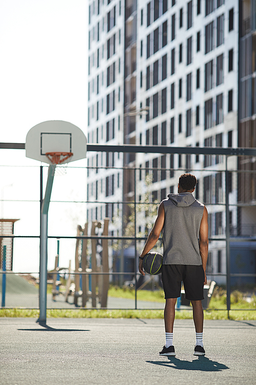 Back view portrait of African basketball player standing by hoop in outdoor court ready to practice, copy space