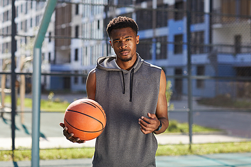 Waist up portrait of African basketball player posing in outdoor court and , copy space