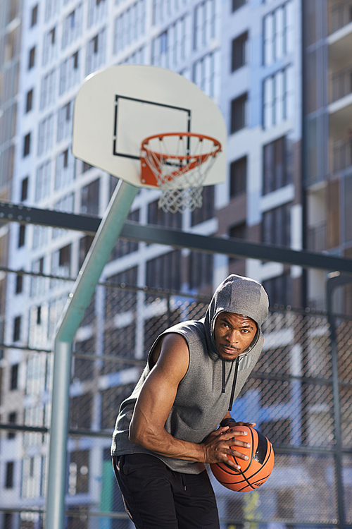 Portrait of muscular basketball player  holding ball in outdoor court, action shot