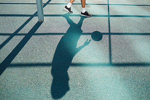 Shadow of unrecognizable man playing basketball in outdoor court, sports background, copy space