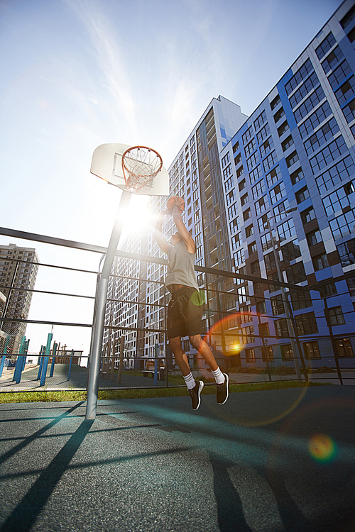 Action shot of African basketball player shooting slam dunk in outdoor court, lens flare