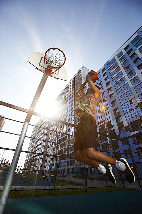 Low angle action shot of African basketball player shooting slam dunk in outdoor court, copy space