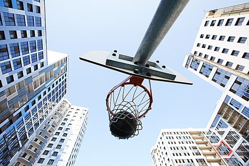 Low angle view of basketball ball shooting through hoop in urban background, copy space