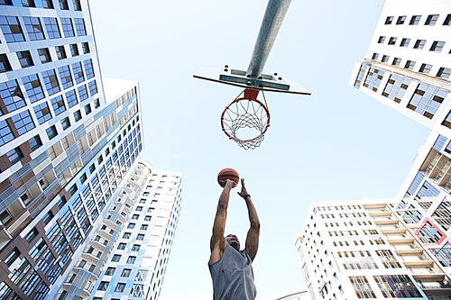 Low angle action shot of African basketball player shooting slam dunk against sky in urban background, copy space