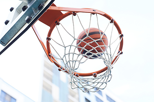 Closeup of basketball shooting through hoop against urban background, copy space