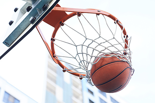 Close up of basketball shooting through hoop against urban background, copy space