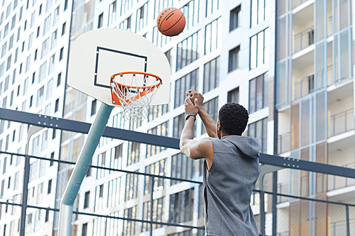 Back view of African man shooting slam dunk in outdoor basketball court in urban setting, copy space