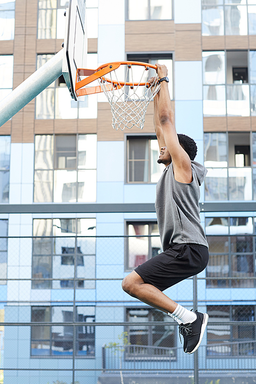 Side view action shot of African basketball player jumping to hoop while training in outdoor court, copy space