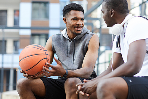 Portrait of two African-American guys chatting sitting on basketball court outdoors, copy space