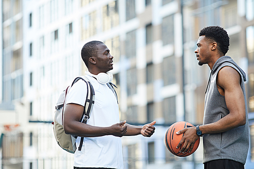Side view portrait of two African-American guys chatting while standing on basketball court outdoors, copy space