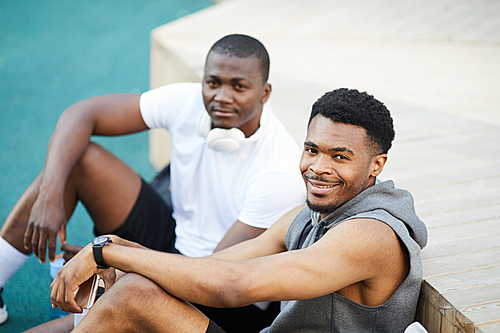 High angle portrait of two African-American guys smiling at camera while chilling in skate park outdoors, copy space