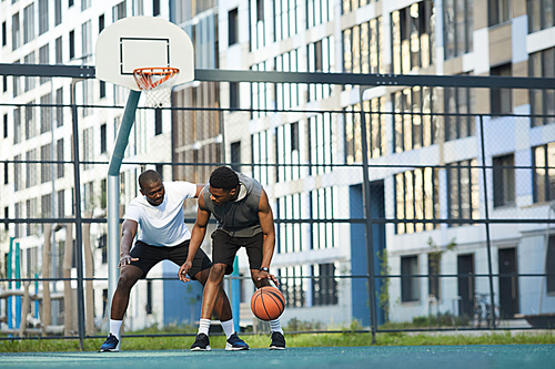 Full length action shot of two African-American guys playing basketball in outdoor court in urban setting, copy space