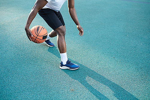Low angle action shot of African-American man playing basketball outdoors, copy space