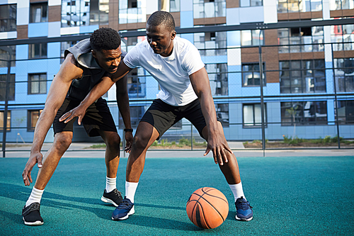 Full length action shot of two muscular African man playing basketball in urban setting, copy space
