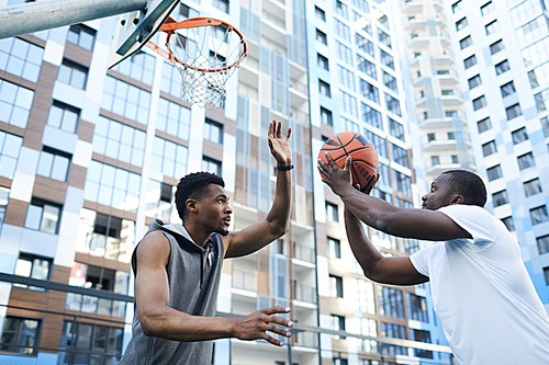 Two sportive African-American men playing basketball in urban setting, copy space