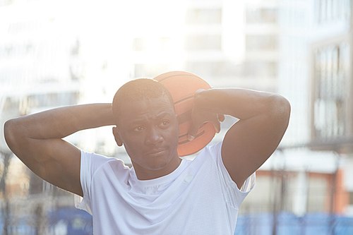 Portrait of contemporary African man posing with basketball ball in outdoor setting, lit by sunlight