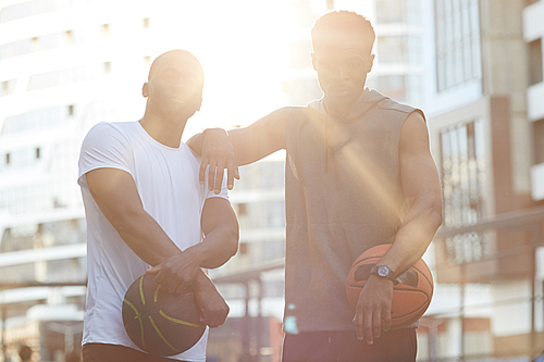 Waist up portrait of two handsome African men posing in basketball court outdoors, lit by sunlight