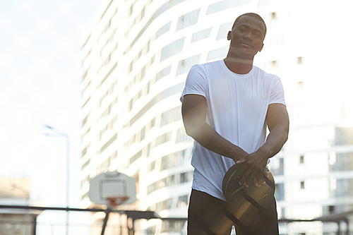 Waist up portrait of handsome African man posing in basketball court outdoors, copy space