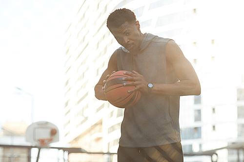 Waist up portrait of handsome African man holding ball while standing in basketball court outdoors, copy space