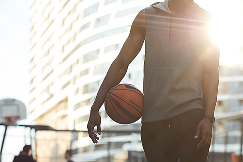 Mid-section portrait of handsome African man holding ball while standing in basketball court outdoors, copy space