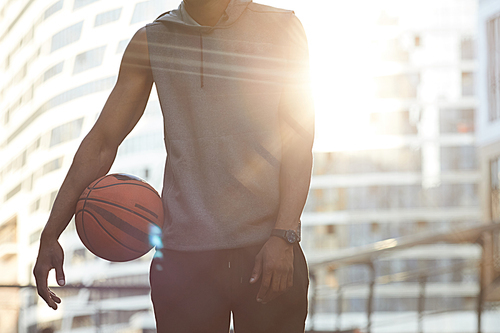 Mid-section portrait of handsome African man holding ball while standing in basketball court lit by sunlight, copy space