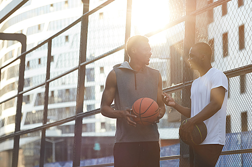 Portrait of two contemporary African men chatting while standing in basketball court outdoors, copy space