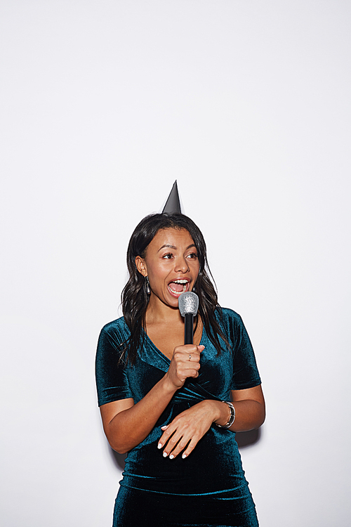 Waist up portrait of young African-American woman singing karaoke while enjoying party, shot with flash over white background