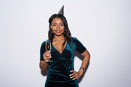 Waist up portrait of elegant African-American woman holding champagne glass while posing against white background at party, shot with flash