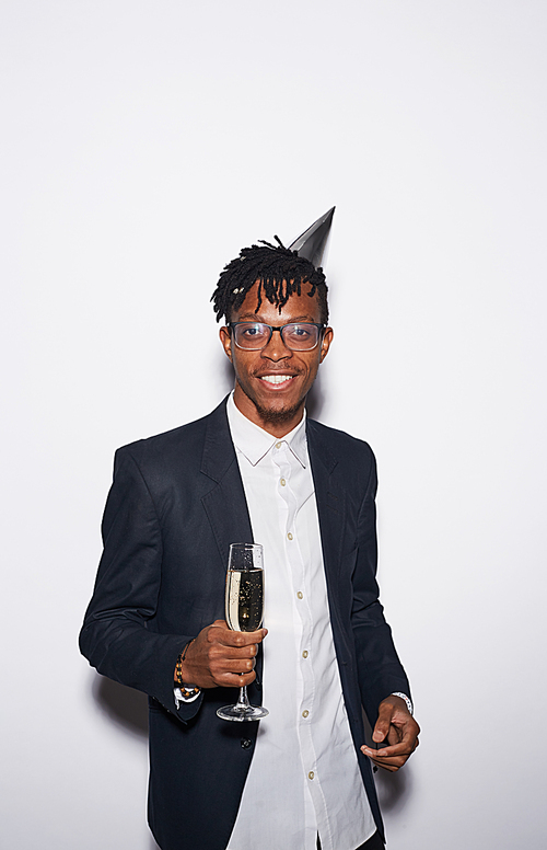 Waist up portrait of trendy African-American man holding champagne glass while posing against white background at party, shot with flash
