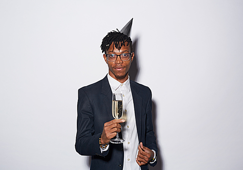 Waist up portrait of trendy African-American man holding champagne glass to camera while posing against white background at party, shot with flash