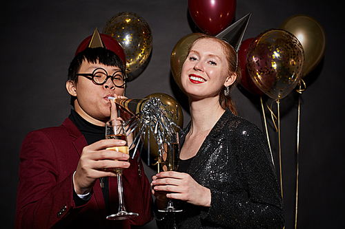 Waist up portrait of young couple clinking champagne glasses while posing over black background enjoying party, shot with flash