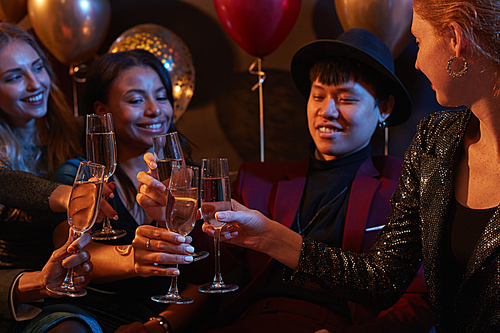 Waist up portrait of multi-ethnic group of elegant young people clinking champagne glasses during party in nightclub
