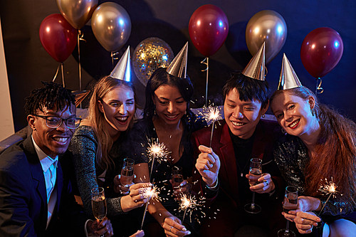 Multi-ethnic group of elegant young people lighting sparklers while celebrating Christmas during party in nightclub, copy space
