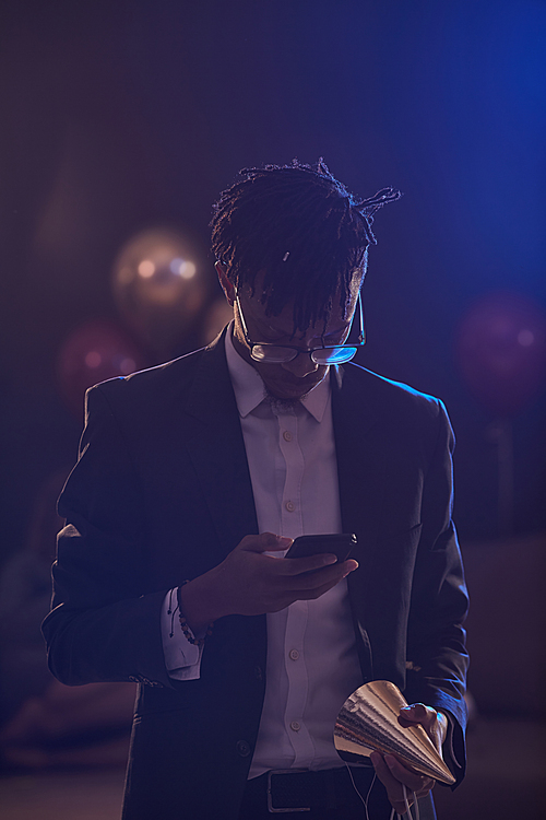 Waist up portrait of elegant African-American man checking smartphone messages in dimly lit room at night club, copy space