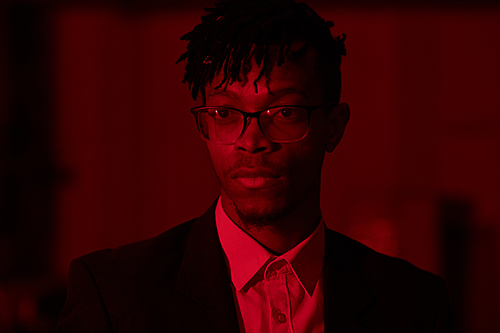 Head and shoulders portrait of trendy African-American man wearing glasses posing looking away in red lighting, copy space