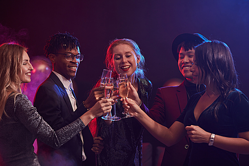 Multi-ethnic group of elegant young people clinking champagne glasses while celebrating at party in smoky night club, copy space