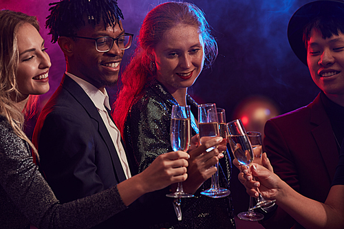 Waist up portrait of young people clinking champagne glasses in smoky night club while celebrating holidays at party, copy space